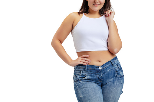 Cropped image of plus-size woman wearing white t-shirt and jeans posing isolated on white studio background. Body positive, weight loss, beauty and equility concept. Copy space for ad