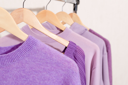 Closeup of fashionable tops in trendy purple, very peri, lavender colors on a shopping rail. Textures, fabrics variety. Sustainability, overconsumption, circular economy concept.