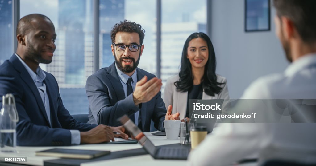 Multi-Ethnic Office Conference Room Meeting: Diverse Team of Top Managers Talk, Brainstorm, Use Computers. Businessman Presenting Investment Strategy to Partners. Close-up Portrait 25-29 Years Stock Photo