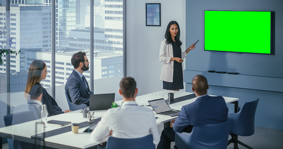 Diverse Office Conference Room Meeting: Asian Female Project Manager Uses Green Screen Chroma Key Wall TV to Present Digital Investment Opportunity for Happy Investment Team.