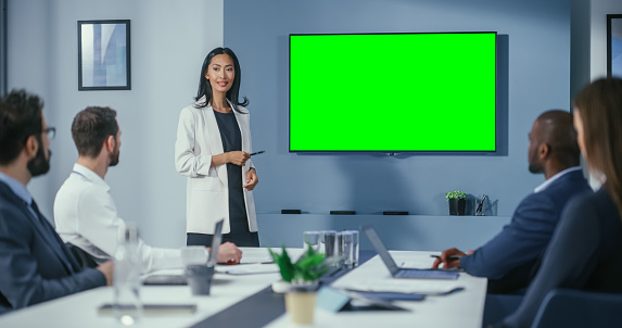 Office Conference Room Meeting Presentation: Motivated Businesswoman Talks, Uses Green Screen Chroma Key Wall TV. Successfully Presenting e-Commerce Product to Group of Multi-Ethnic Investors