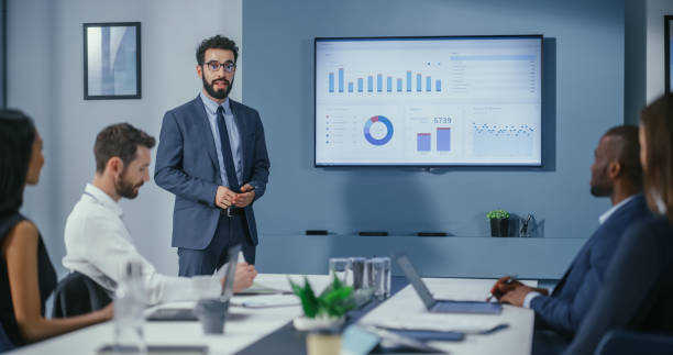 Office Conference Room Meeting: Digital Enterpreneur Presents e-Commerce Investment Strategy for Group of Investors. Wall TV Showing Big Data Analysis, Infographics, Stock Market Information, Trends