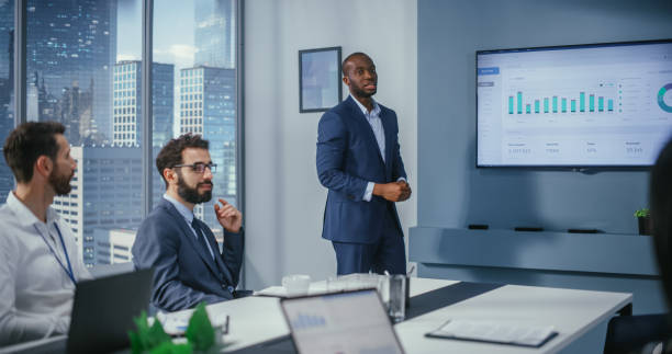 istock Diverse Office Conference Room Meeting: Successful Black Executive Director Presents e-Commerce Fintech Growth Statistics to a Group of Investors. Wall TV with Big Data Analysis, Infographics 1360337490