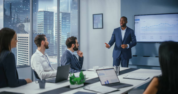 istock Diverse Office Conference Room Meeting: Charismatic Black Digital Entrepreneur Presents e-Commerce Fintech Growth Statistics to a Group of Investors. Wall TV with Big Data Analysis, Infographics 1360337501