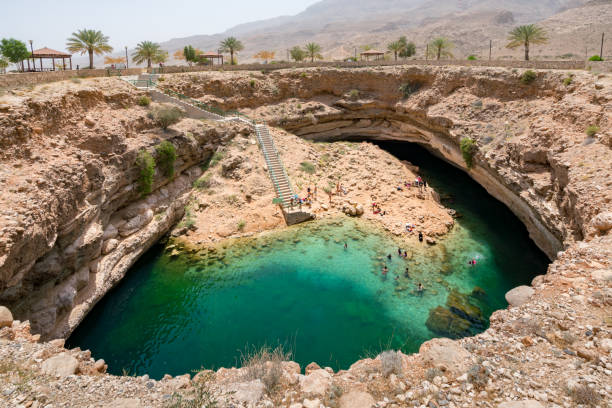 People swimming and hanging around turquoise waters of Bimmah Sinkhole pool, or Hawiyyat Najm, sea water lagoon in Omanian desert. stock photo