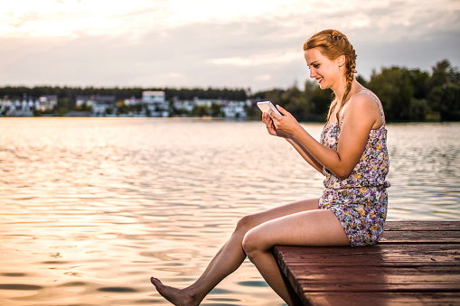Young woman relaxing on lake pier while using her digital tablet