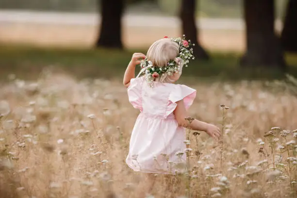 Portrait of a little beautiful girl on nature on summer day vacation. child in red dress is playing in the green grass at the sunset time. The concept of family holiday and time together
