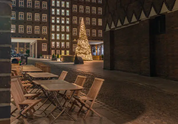 Chilehaus in the Kontorhaus quarter with Christmas tree, Hamburg, Germany. Advent time by Chilehaus in Hamburg at Corona time. Chairs in front of tables in an outdoor cafe.