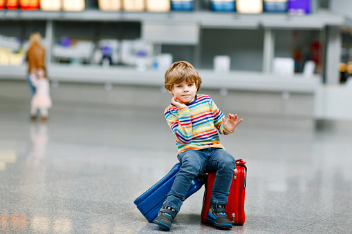 Happy little kid boy with big suitcase luggage at terminal on international airport. Preschool excited child wait for flight and going on vacations. Travel family lifestyle