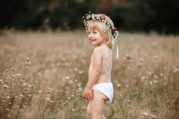 little beautiful girl on nature on summer day vacation. childgirl in panties and a flowers wreath on her head is playing in the field on summer day. The concept of family holiday and time together.