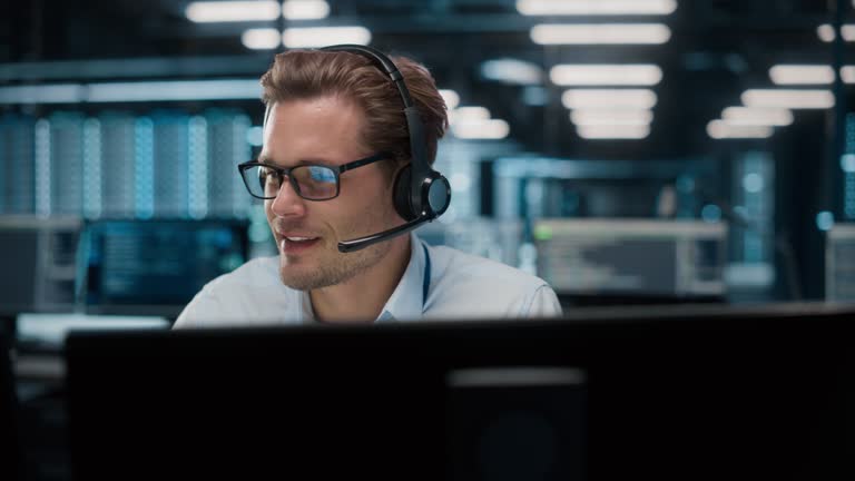 Call Center Office: Portrait of Friendly Caucasian Male Technical Customer Support Specialist Talking on a Headset, uses Computer. Client Experience Officer Helps Online via Video Conference