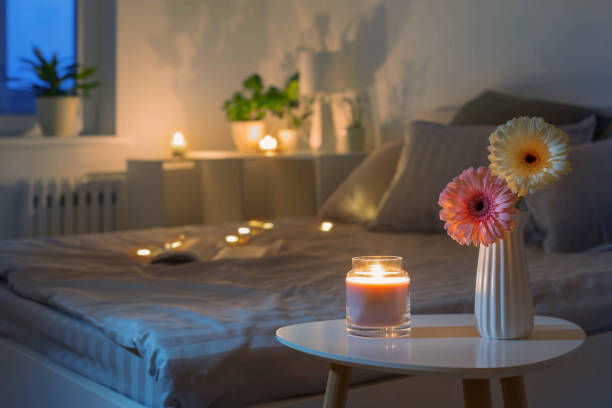 gerbers in white vase with burning candle in bedroom  in evening stock photo