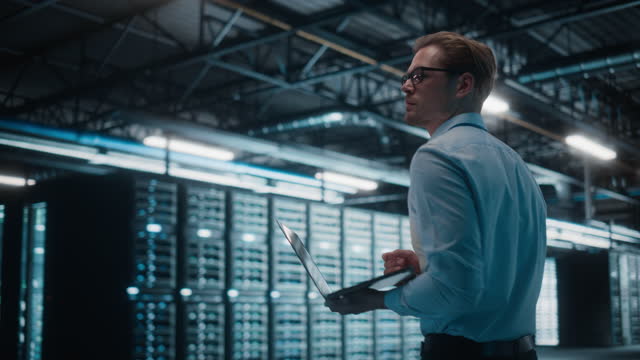 Male IT Specialist Using Tablet Computer in Data Center, Walking Through Big Data Center. Cloud Services Server, Computing Facility. Successful e-Business Digital Entrepreneur or System Administrator