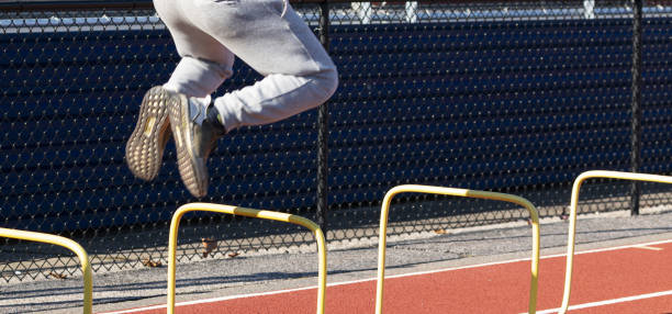 istock Boy jumping over yellow two foot tall plastic hurdles in front o 1360346623