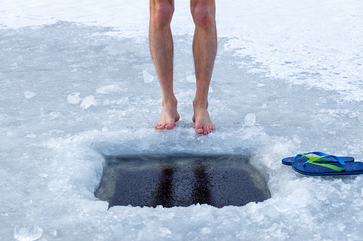 Man and ice hole. Legs and ice hole close-up. Health and cold water hardening concept.
