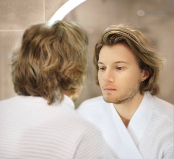 istock young man looking in the mirror,combing his hair,looking at problems on face 1360350609