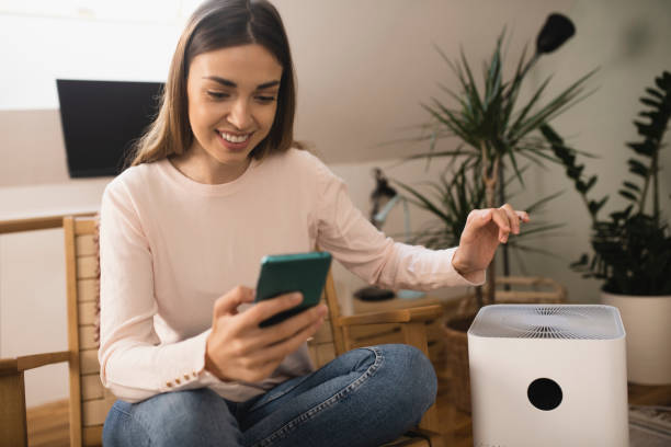 istock Happy young woman turning on air purifier using a smartphone 1360351263