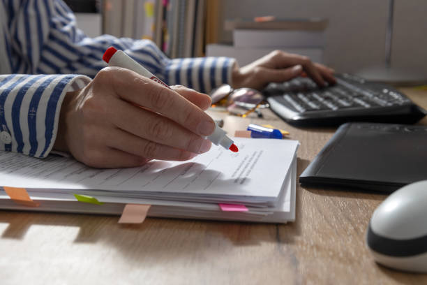 gros plan de la main d’une femme qui tient un marqueur rouge et qui trôde du texte pour la grammaire et l’utilisation de l’ordinateur. table et documents de bureau, clavier, souris, tablette, pile de livres dessus - linguist photos et images de collection