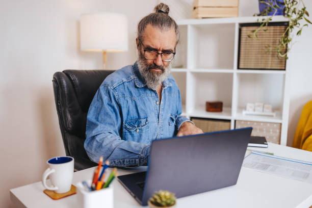 istock Mature male architect work with blueprints and laptop from home office 1360353579
