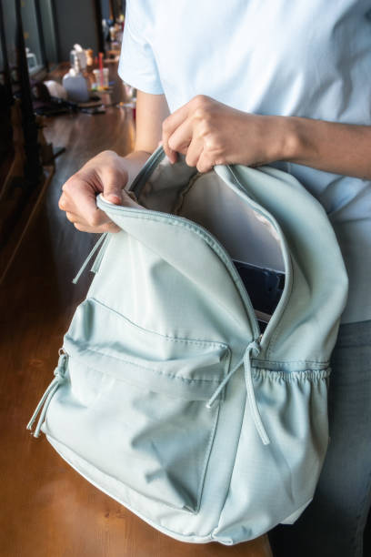Close-up of the hand of a young female student packing a blue backpack with belongings to college or university Close-up of the hand of a young female student packing a blue backpack with belongings to college or university. Collecting things for a trip, vacation. satchel stock pictures, royalty-free photos & images