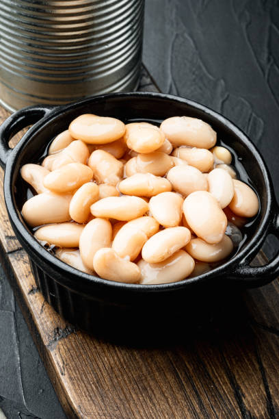 istock Canned white beans, with metal can, in bowl, on black stone background 1360362473