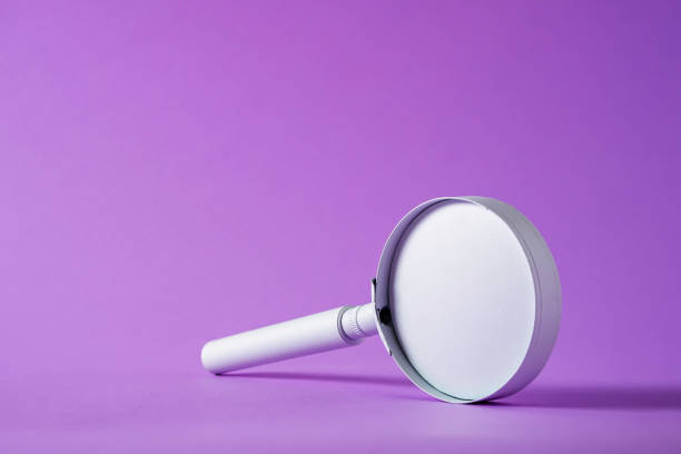 istock Magnifying glass balanced on edge over graduated purple 1360363391