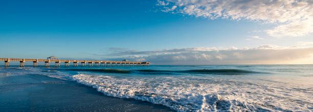 Florida beach with beautiful waves and sea foam on the sand. Beautiful cloudy sky over a pier.  Juno Beach, Florida, USA. Image for banner or web header.