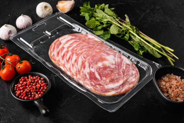 istock Sliced dry cured sausage in vacuum pack, on black dark stone table background 1360365907