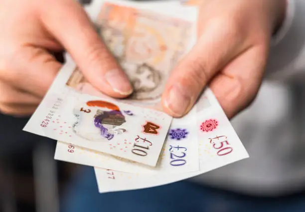 Close-up of a woman holding modern polymer ten, twenty and fifty pound notes.