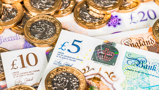 UK five, ten and twenty pound banknotes, with one pound coins in close-up.