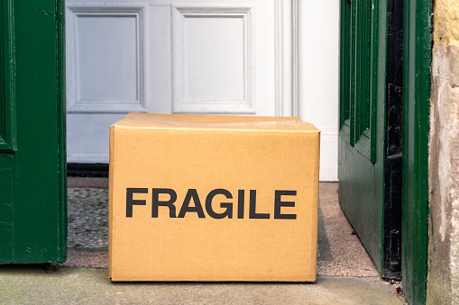 'Fragile' printed on a cardboard box delivery left on the front porch of a house.