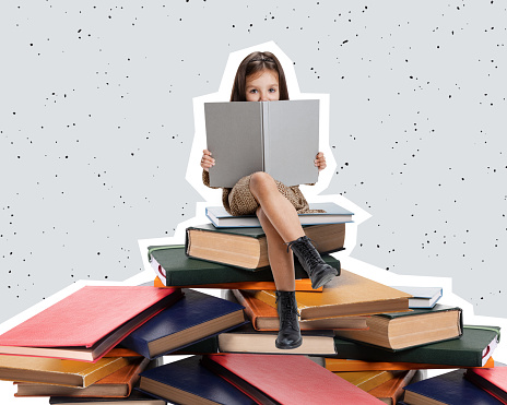Creative design curious little girl, child sitting on stack of books and reading isolated over gray background. Concept of education, childhood, imagination, discovery, artwork, inspiration and ad