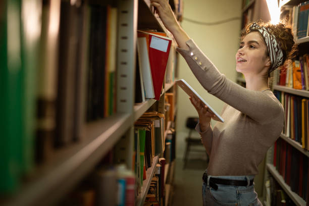 istock Young student holding tablet and searching book at library 1360367283