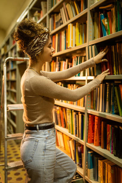 istock Young librarian picking book from bookshelf 1360367560