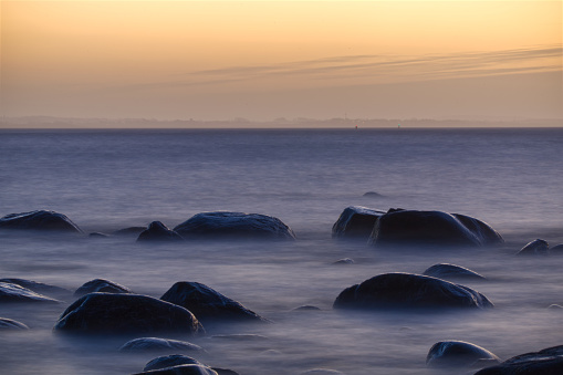 Long exposure photography of rocks at the western coast of Sweden, Halmstad. Morning light. No people. Plenty copy space. Red sky and horizon visible in the background