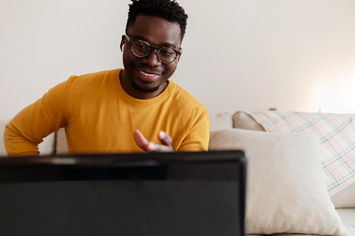 Attractive young African man using laptop and smiling while sitting indoors. Portrait of a young African-American freelancer working from his home office. Technology concept.