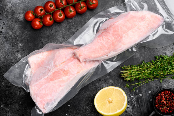 Red Snapper frozen pack fish meat, with herbs, on black dark stone table background, top view flat lay