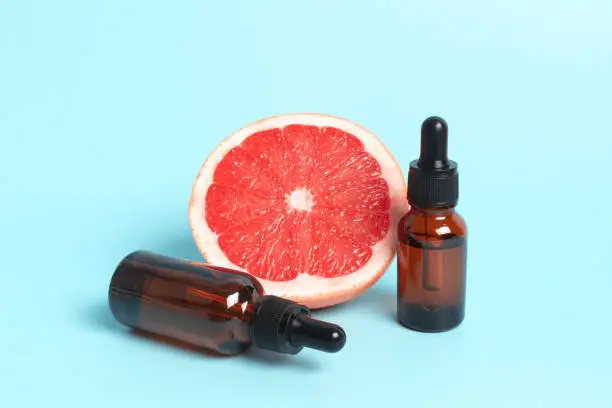Bottle of grapefruit essential oil on light blue background