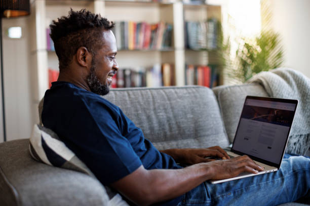 Relaxed smiling man sitting on sofa and using laptop stock photo