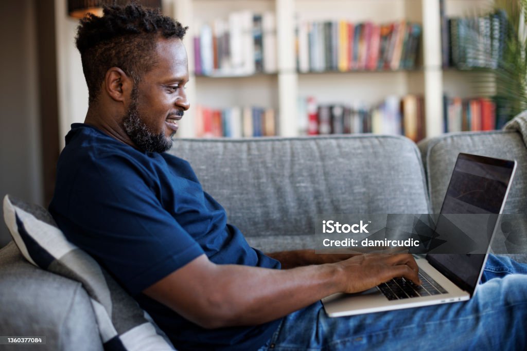 Relaxed smiling man sitting on sofa and using laptop Questionnaire Stock Photo