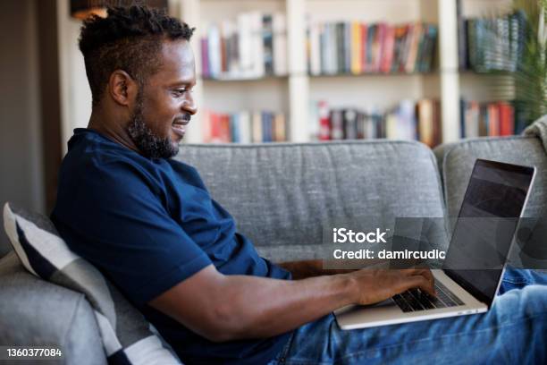 Relaxed Smiling Man Sitting On Sofa And Using Laptop Stock Photo - Download Image Now
