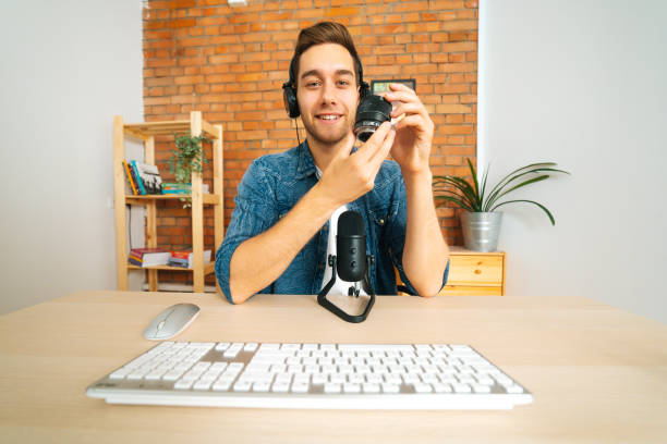 front view of cheerful male blogger broadcaster streaming live podcast recording review of camera lens using professional microphone. - camera lens home video camera broadcasting imagens e fotografias de stock