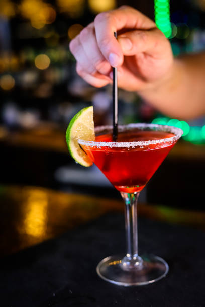 istock In a funnel-shaped glass on a long stem, a two-tone cocktail, dark red below, translucent white above, a lime slice on the edge of the glass. Filming of the bar menu against the background of bright lights in bokeh. 1360380059