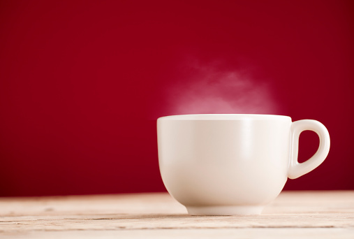 Cup of coffee with hot steam, front view, on table, red background