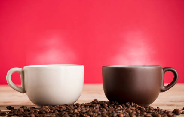 2 cups of hot steamed coffee with beans, on table, red background
