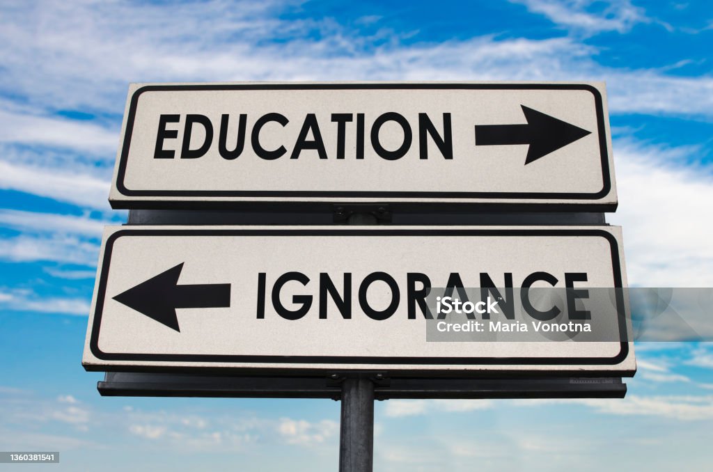 Education versus ignorance road sign Education versus ignorance road sign with two arrows on blue and grey sky background. White two street sign with arrows on metal pole. Two way road sign with text. Ignorance Stock Photo
