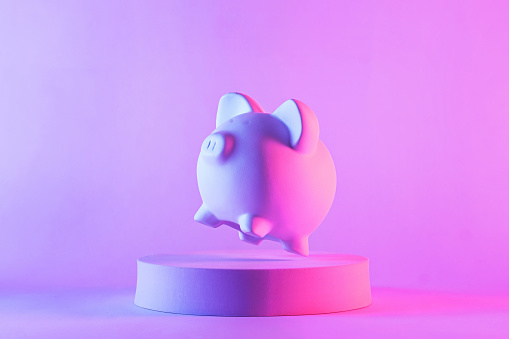 Studio close-up of piggy bank floating above a round podium against purple blank background for copy space as symbol for quality saving money