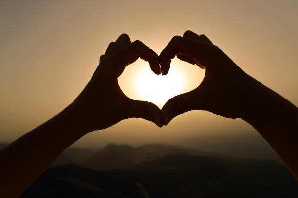 istock Woman hands silhouette framing sun making heart shape 1360382591