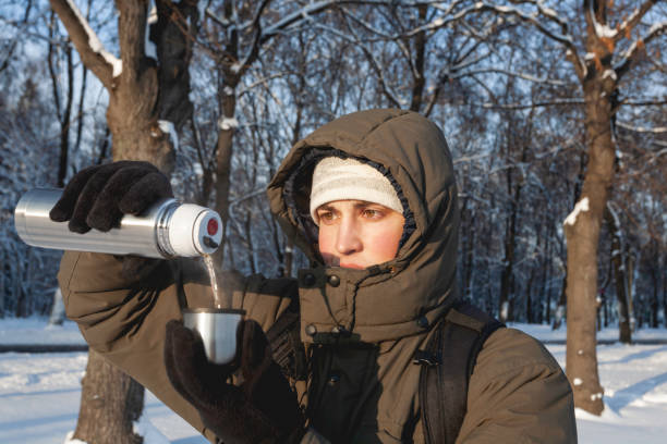 istock Man drinks hot tea from metal thermos. Leisure activity in winter forest at sunset. 1360386692
