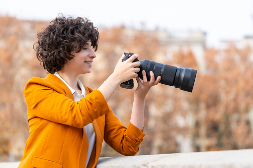 Young brunette woman with curly hair taking a picture with telephoto lens in the street